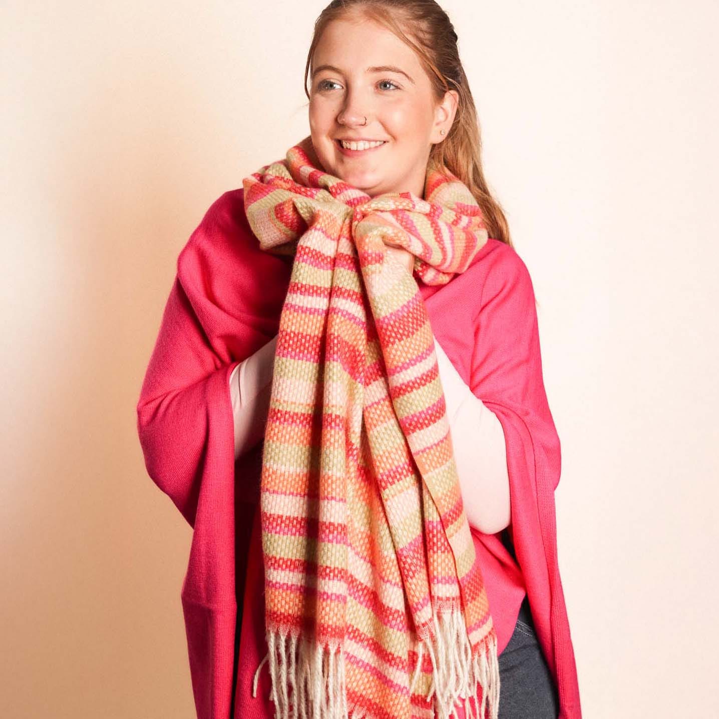 Woman wearing a pink coat and a colorful striped scarf against a beige background