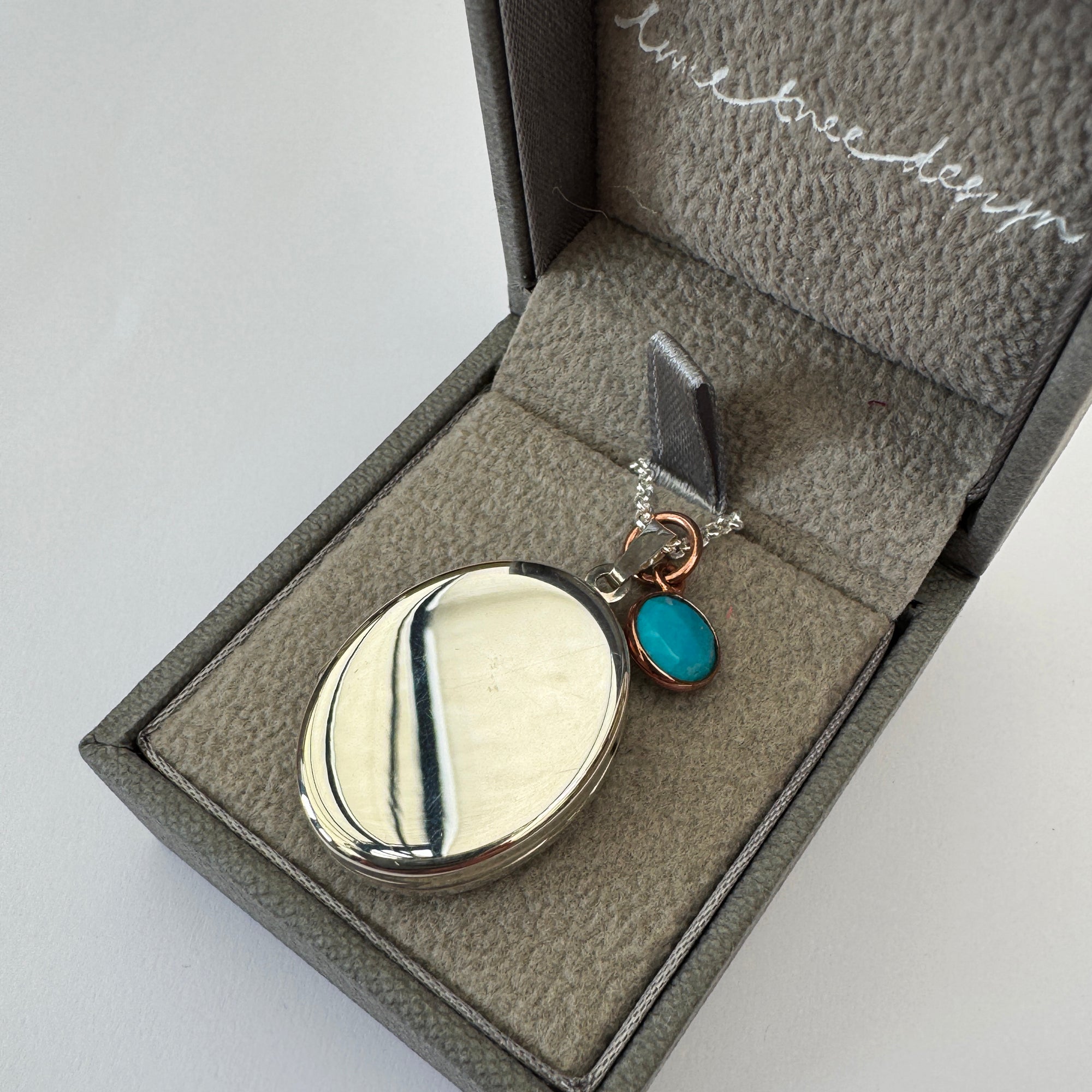 Jewelry box with a silver locket and turquoise stone on a light gray background