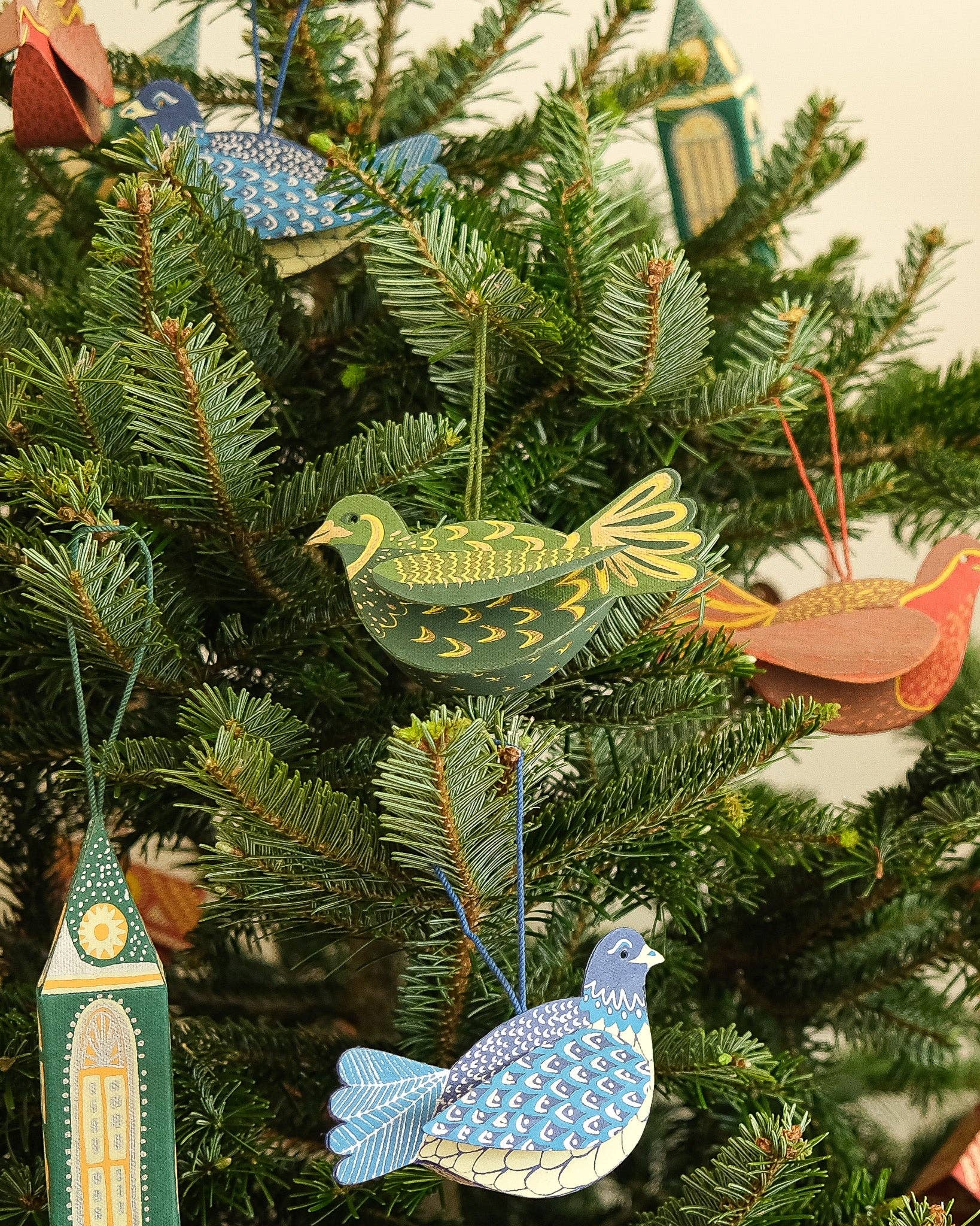Decorative Christmas ornaments on a tree, including birds and a clock tower.