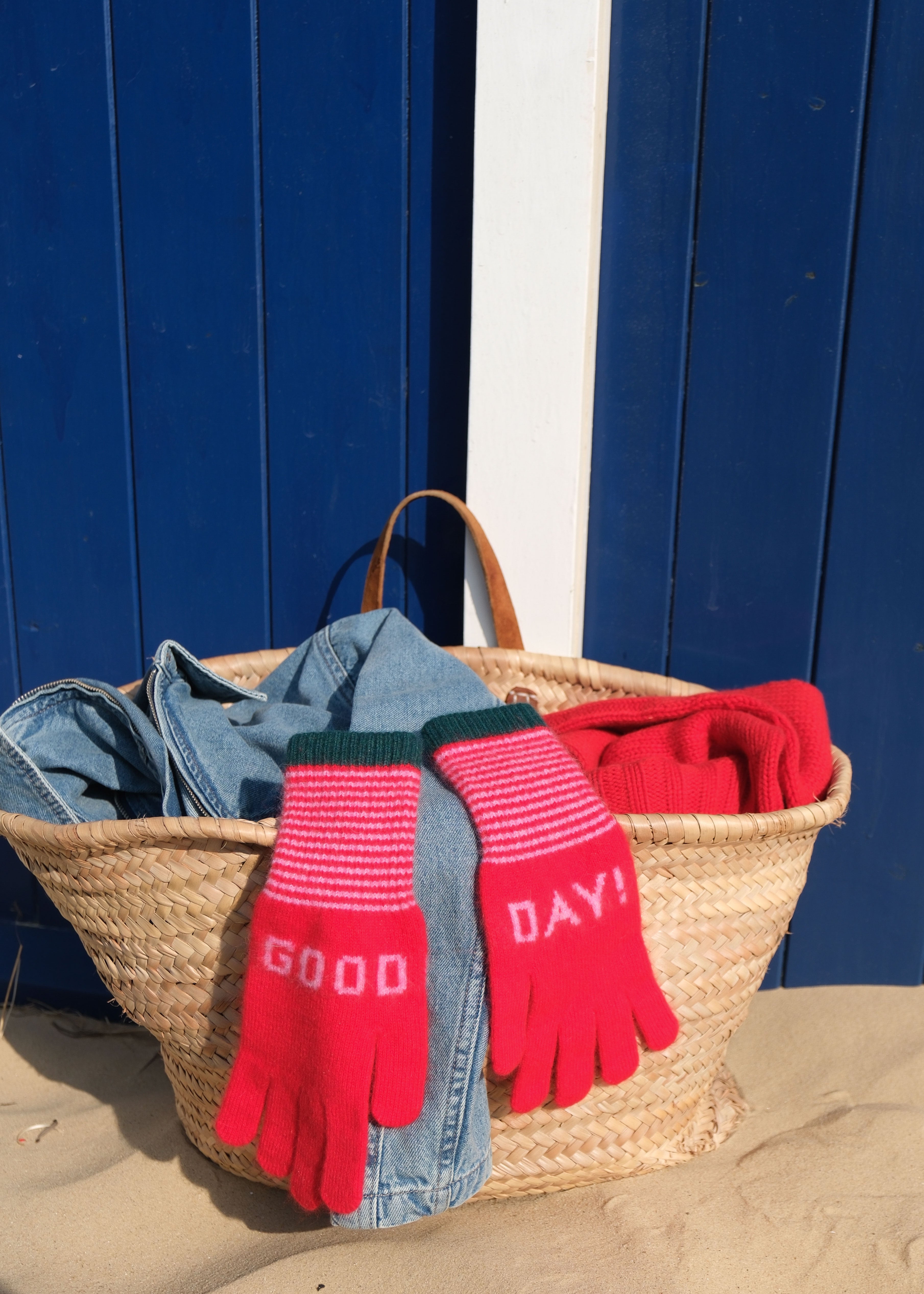 Basket with gloves, denim, and red fabric against a blue wall