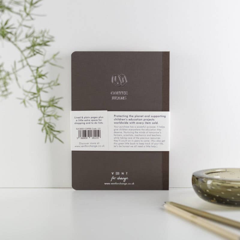Back cover of a notebook with branding and text on a white surface with a plant and candle in the background