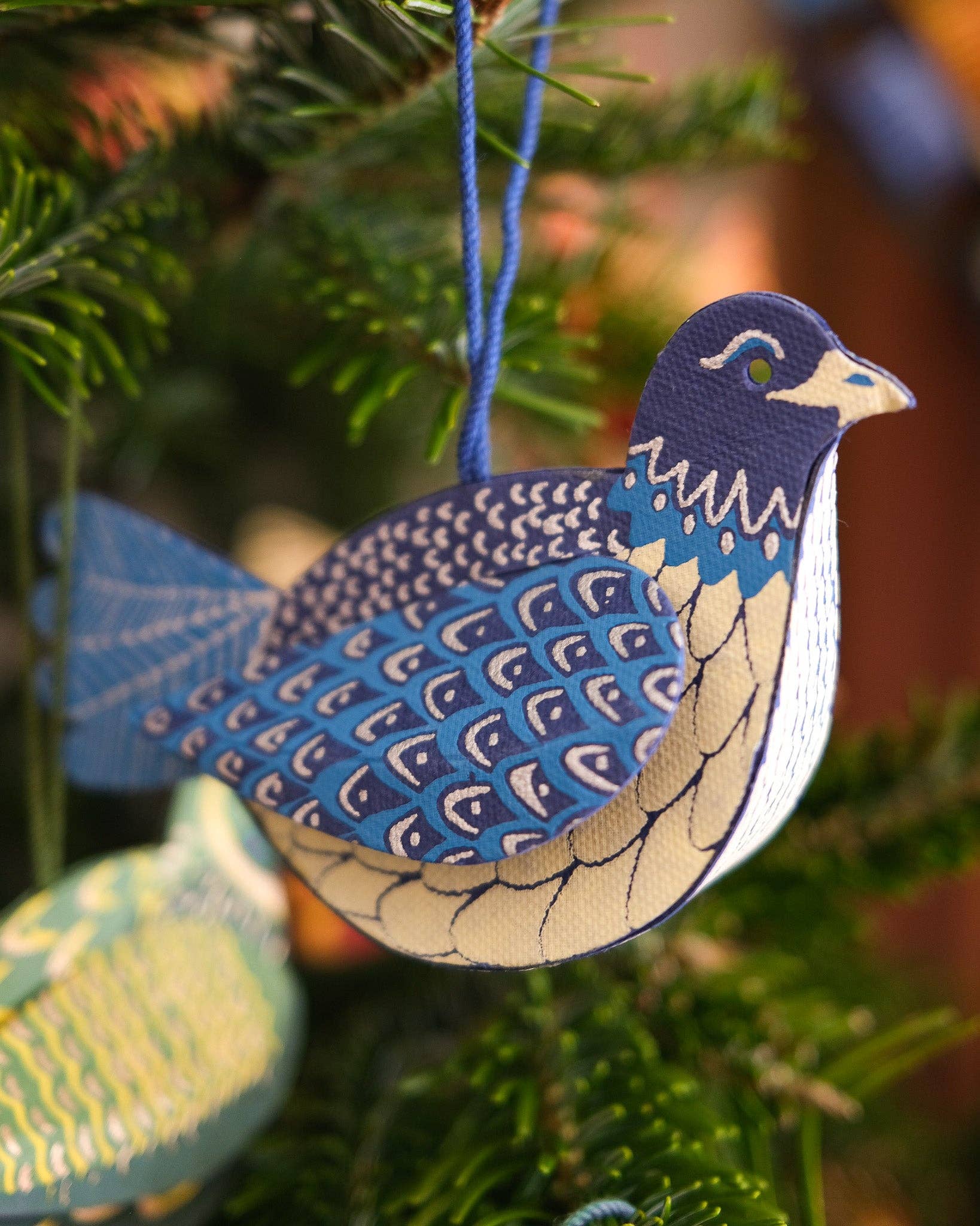 Decorative blue and beige bird ornament hanging on a Christmas tree.