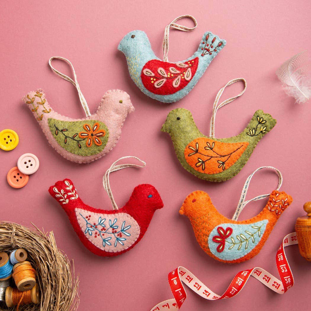 Colorful felt bird ornaments on a pink background with sewing materials.