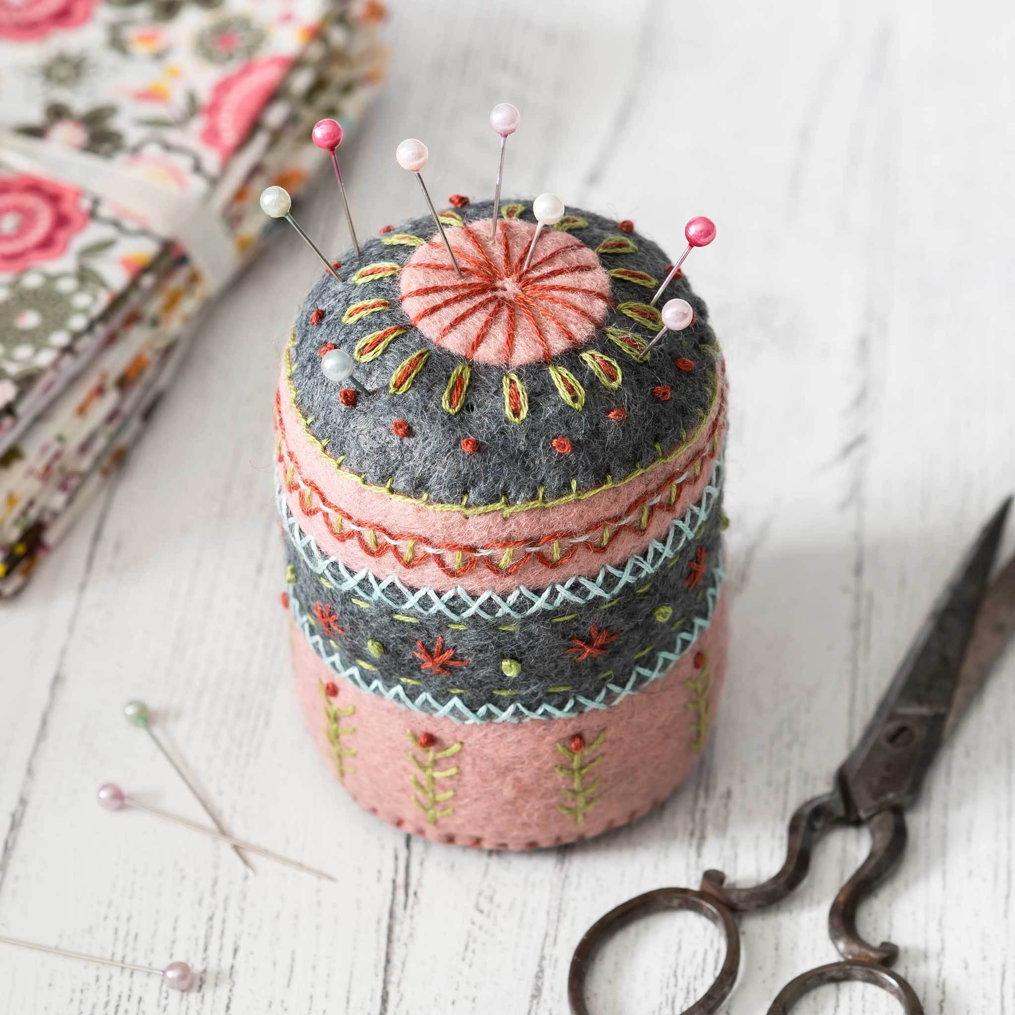 Decorative pincushion with embroidered patterns, pins, and a pair of scissors on a wooden surface.