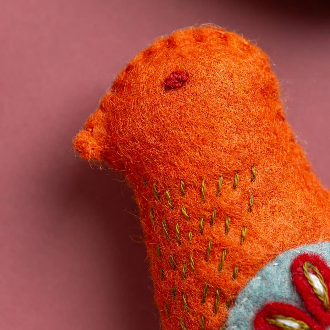 Close-up of an orange knitted or felted animal toy with embroidered details on a pink background