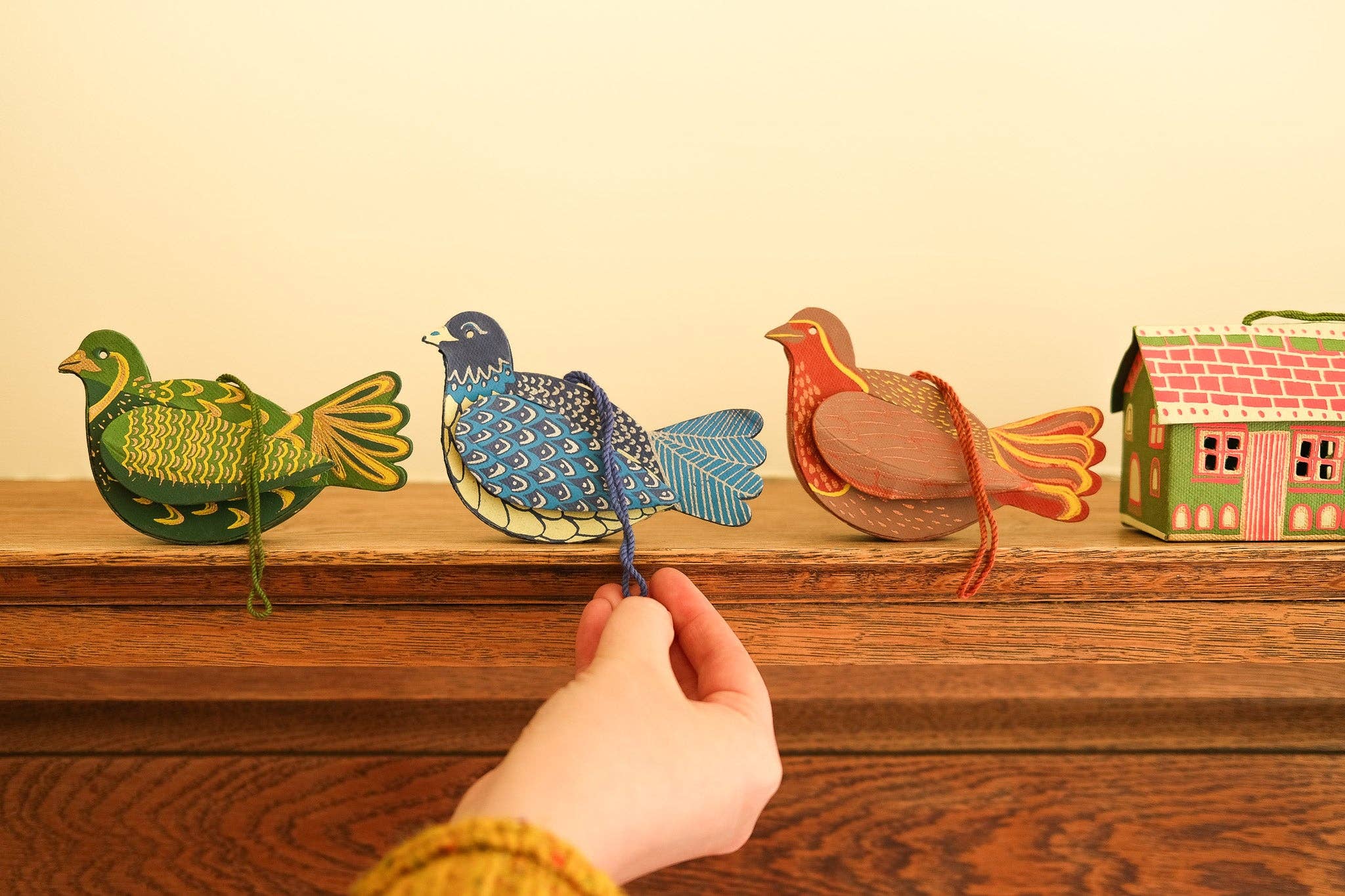 Hand interacting with colorful paper birds and a house on a wooden surface.