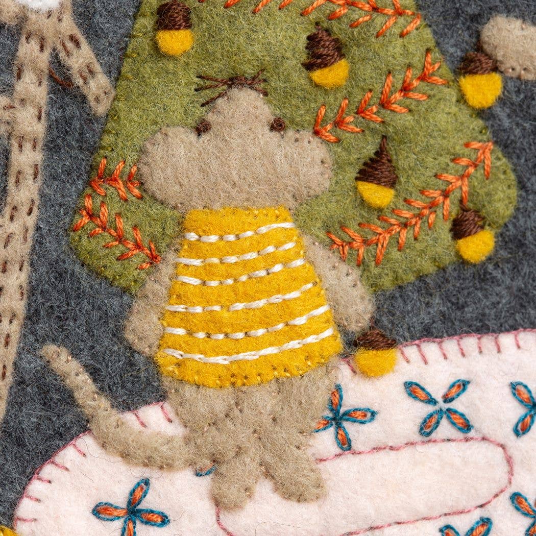 Felted textile art with a dog wearing a yellow sweater and a wreath in the background