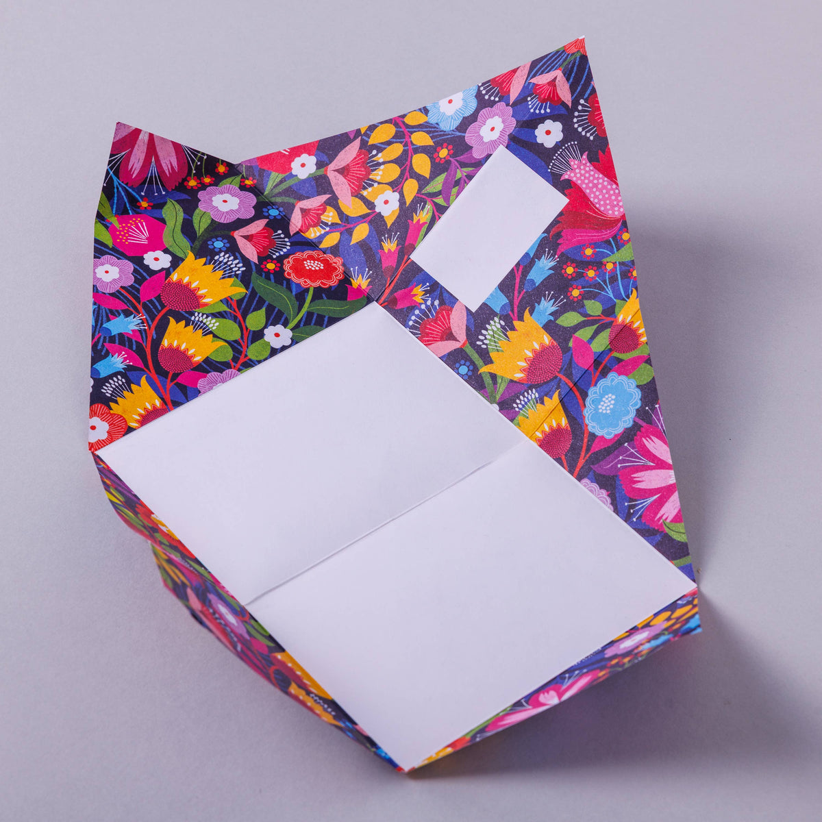 Colourful floral-patterned folded letter paper with a white interior on a grey background