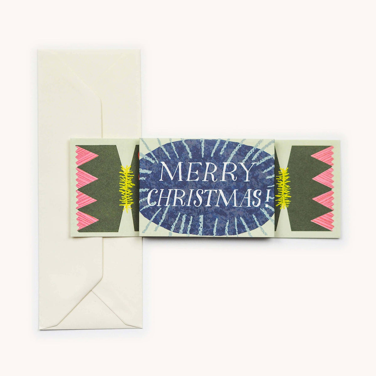 A Christmas card designed like a cracker, shown folded flat with a cream envelope behind it on a light background. The center of the card is blue with white radial lines and the words “MERRY CHRISTMAS!” in white.