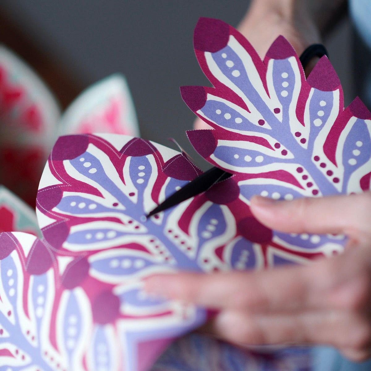 Person cutting out a purple and pink floral paper design with scissors.
