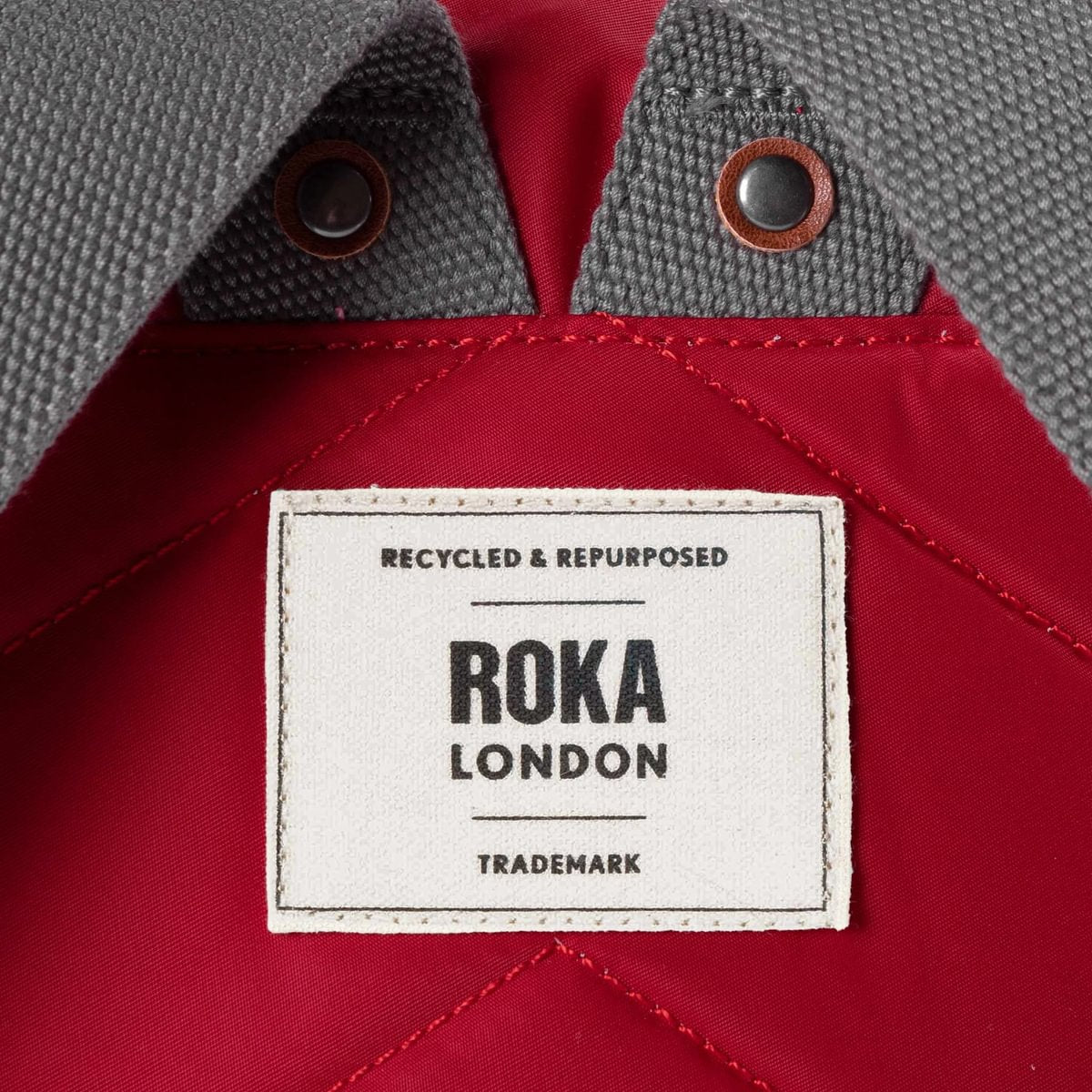 Close-up of a Roka London label on a red and gray fabric background
