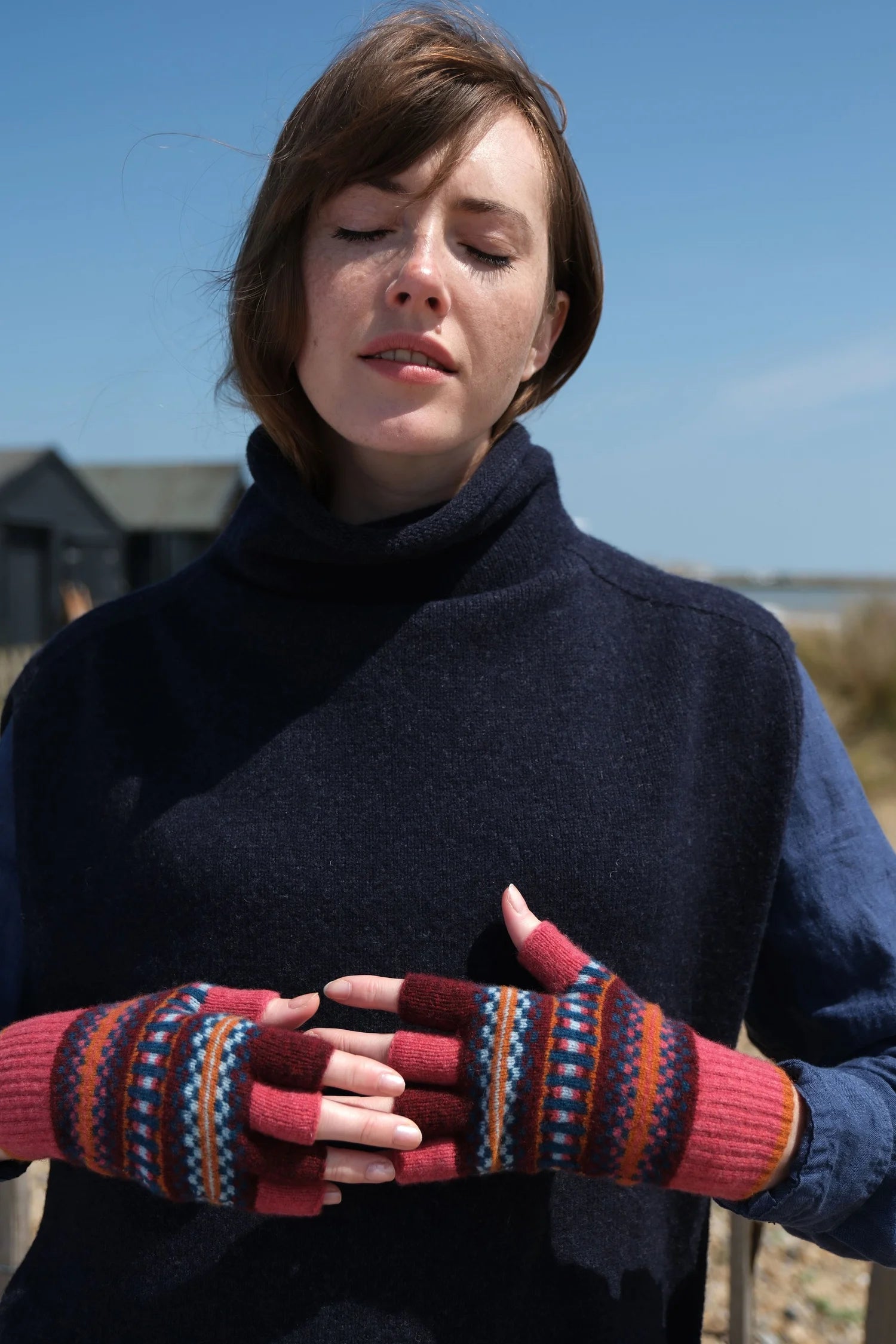 Woman wearing a dark blue sweater and colorful patterned gloves outdoors.
