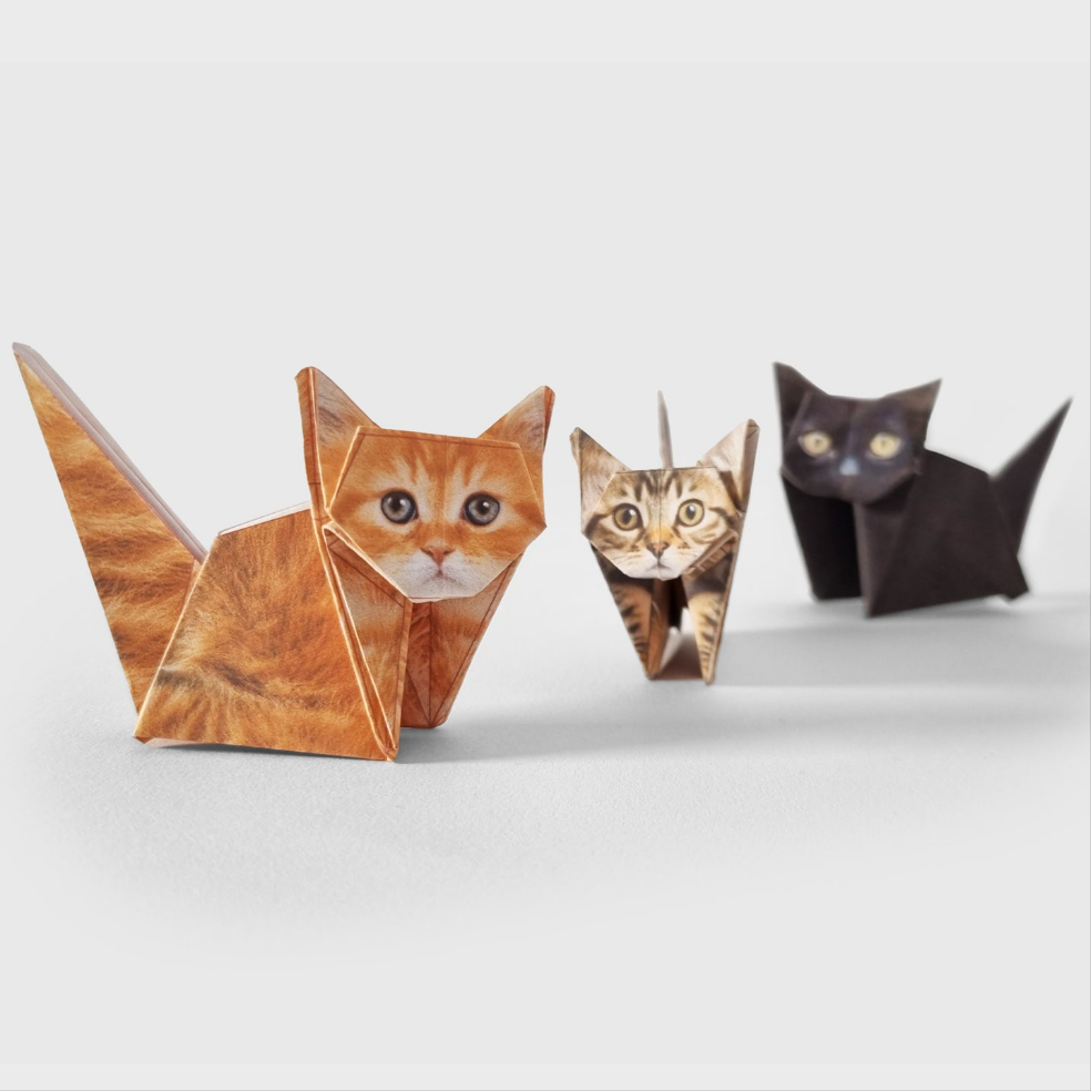 Three folded origami cats. One ginger, one tabby and one black, on a neutral background.