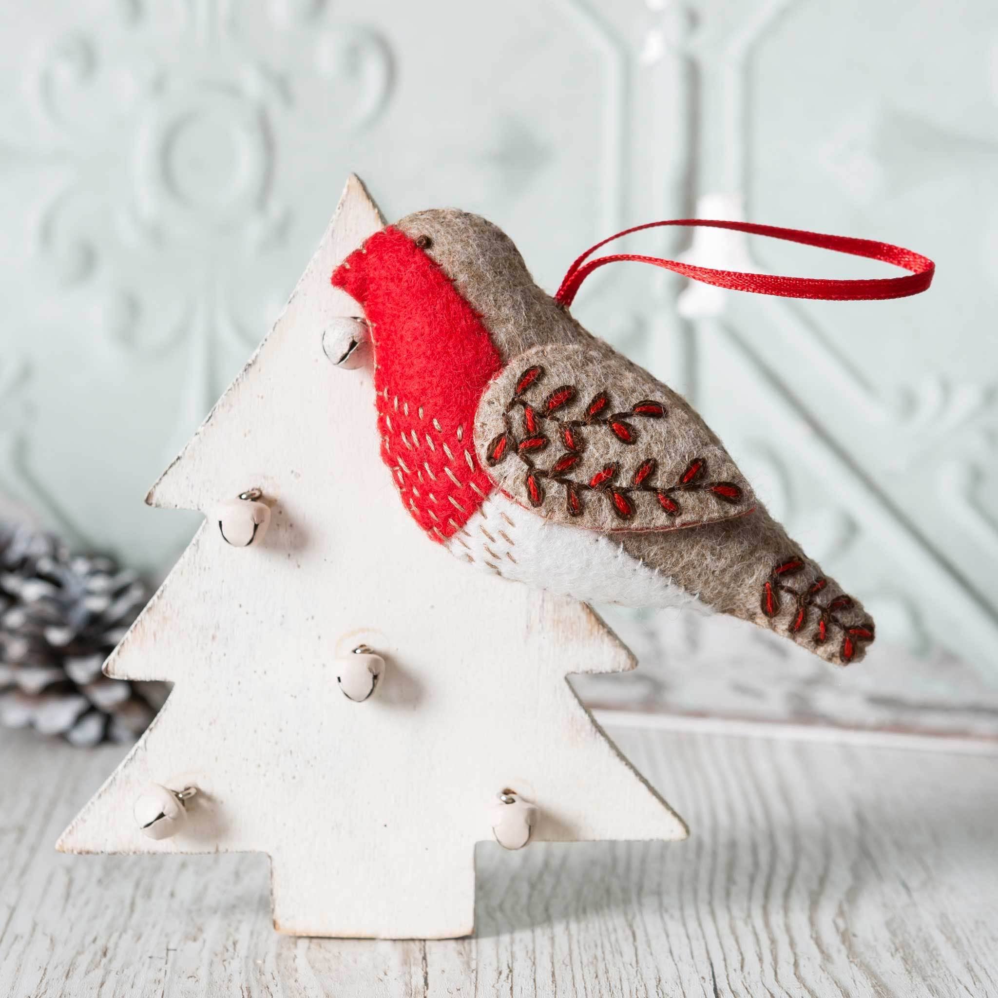 An embroidered red and brown felt robin with red ribbon loop displayed on a rustic scandi style wooden white tree.