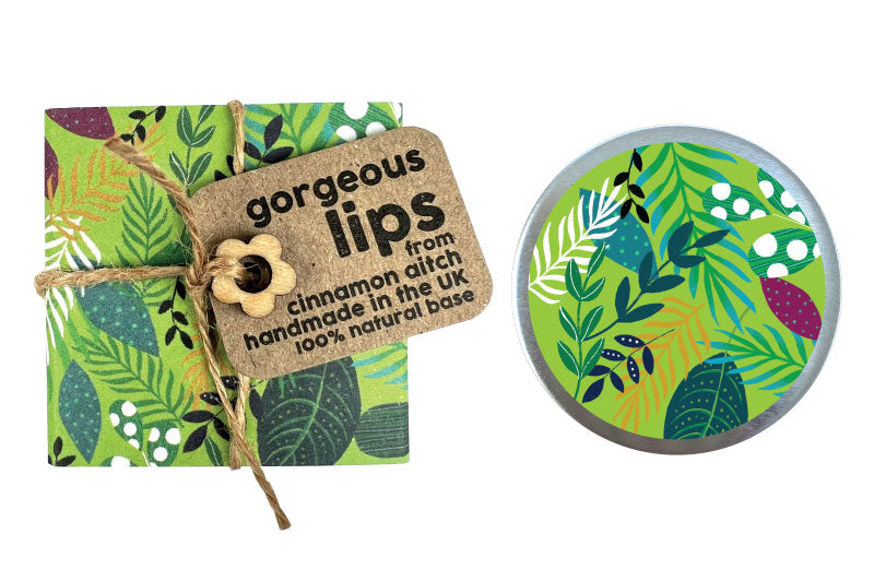 Lip balm with a decorative label and a small round container with a green leaf design on a white background.