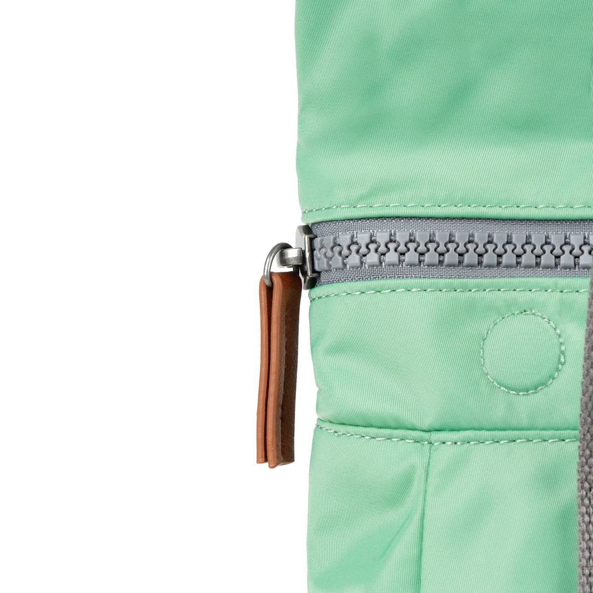 Close-up of a green bag with a grey zipper and brown leather pull tab on a white background