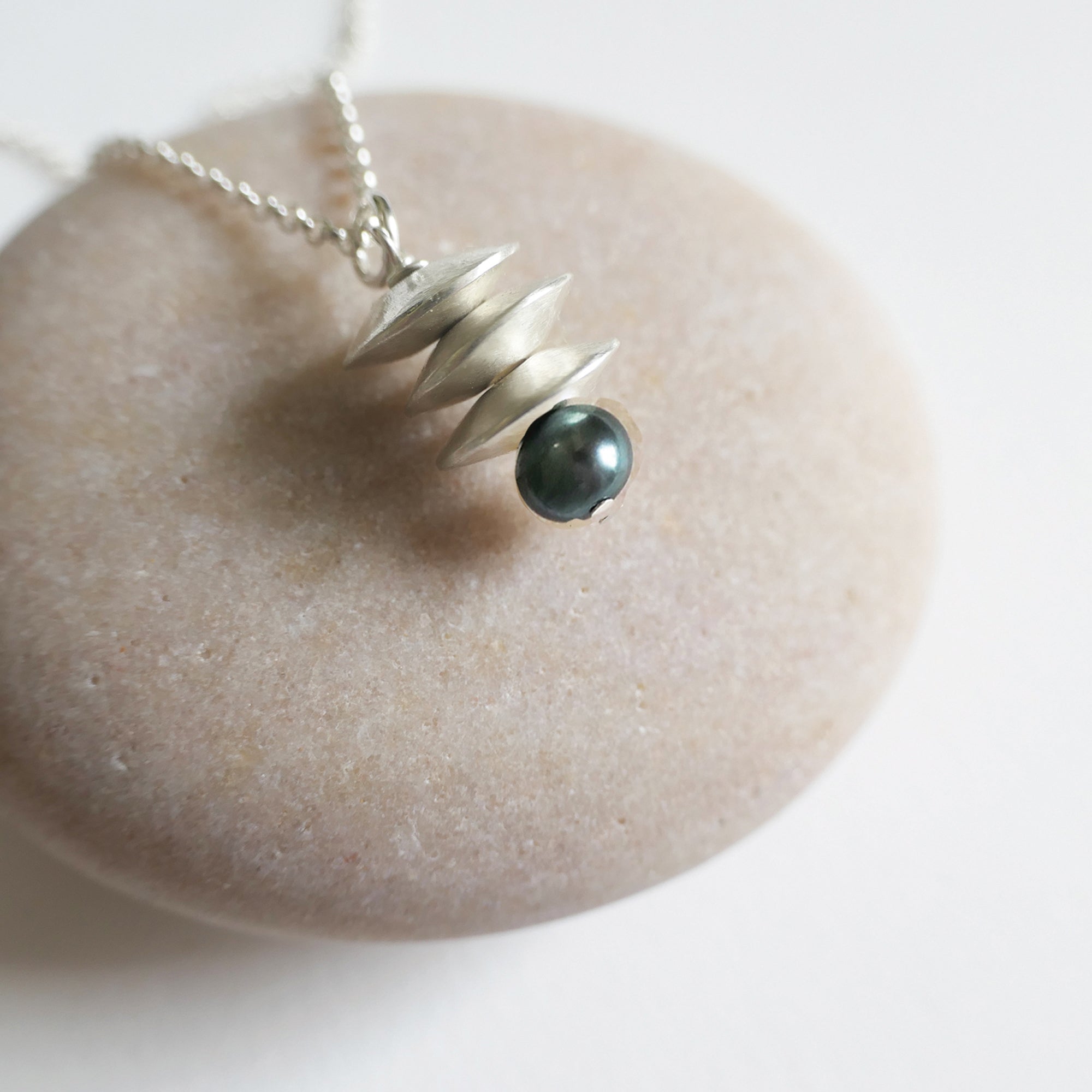 Silver necklace with a dark bead pendant on a light stone surface