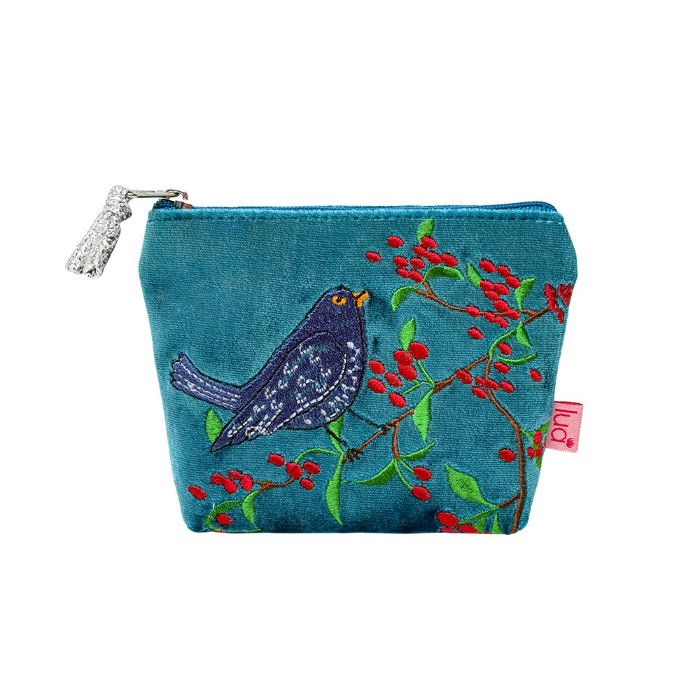 A teal blue fabric zippered pouch featuring an embroidered design of a dark blue bird perched on a branch with red berries and green leaves. The pouch has a silver zipper with a decorative silver pull tab and a small pink fabric tag on the right side.
