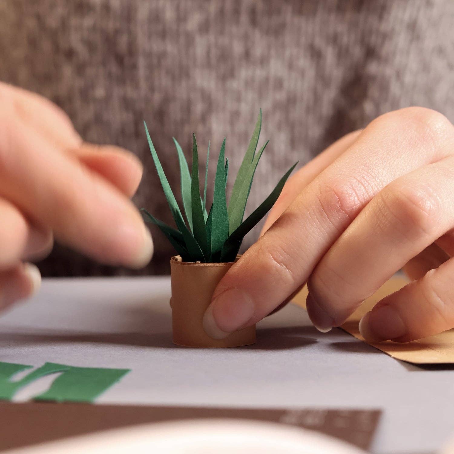 Person holding a small paper plant with brown pot on a neutral background