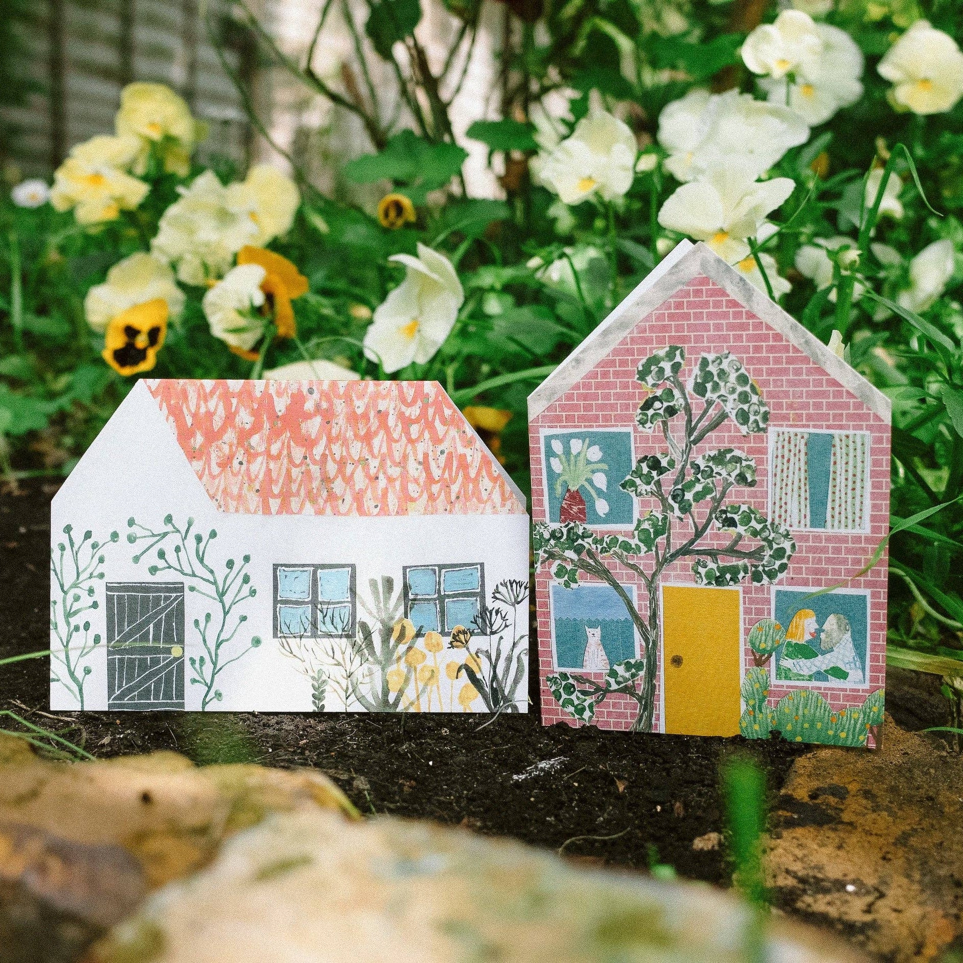 Two house themed cards with colourful designs on a natural background with flowers.