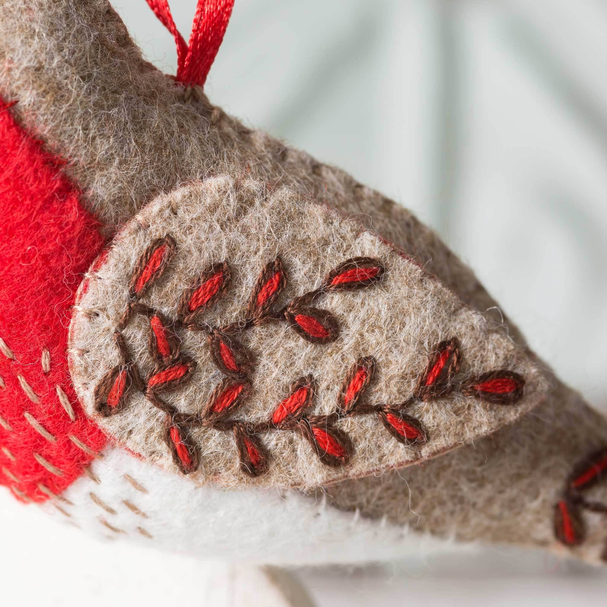 Detail of botanical embroidery on robin wing in brown and red.