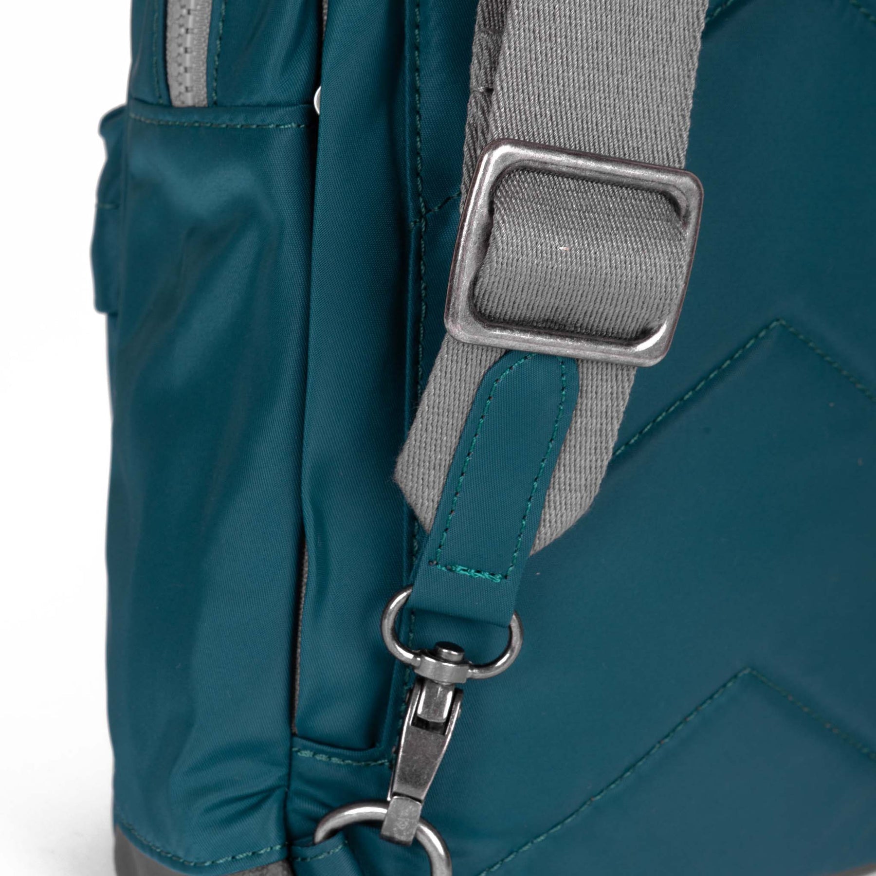 Close-up of a teal backpack with a gray strap and metal buckle on a white background