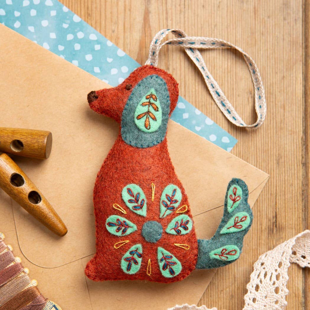 Decorative felt dog ornament with floral patterns on a wooden surface with craft materials.