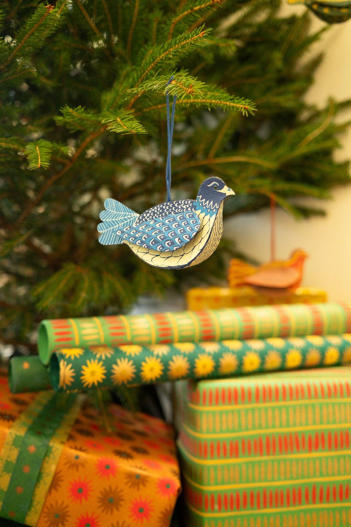 Decorative bird ornament hanging on a Christmas tree with wrapped presents below.