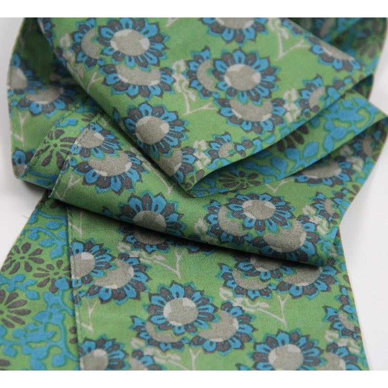 A folded piece of green fabric with a repeating floral pattern in blue, gray, and olive green, shown on a plain white background.
