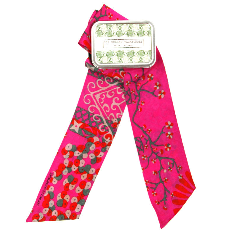 A bright pink silk scarf with a botanical and abstract pattern, tied around a silver metal tin labeled 'Le Petit Vachanxi'.