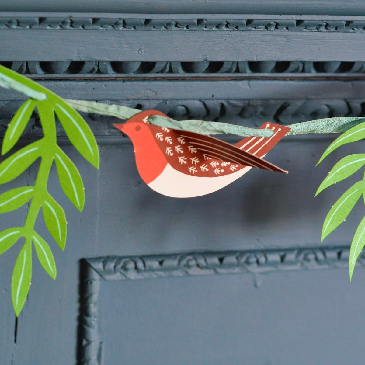 Decorative paper bird on a branch with green leaves against a gray background