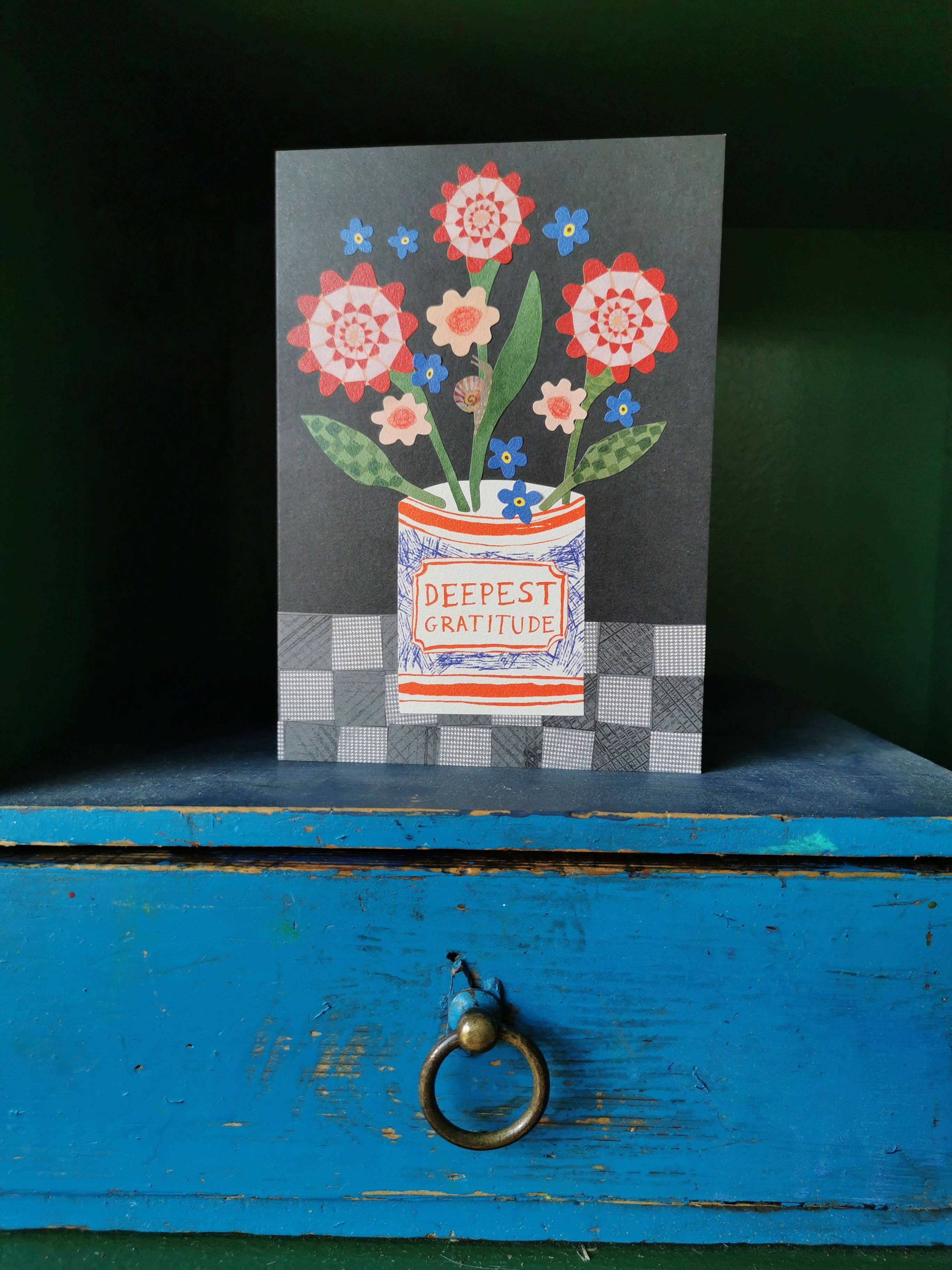 Greeting card with floral design and 'Deepest Gratitude' text on a blue wooden surface.