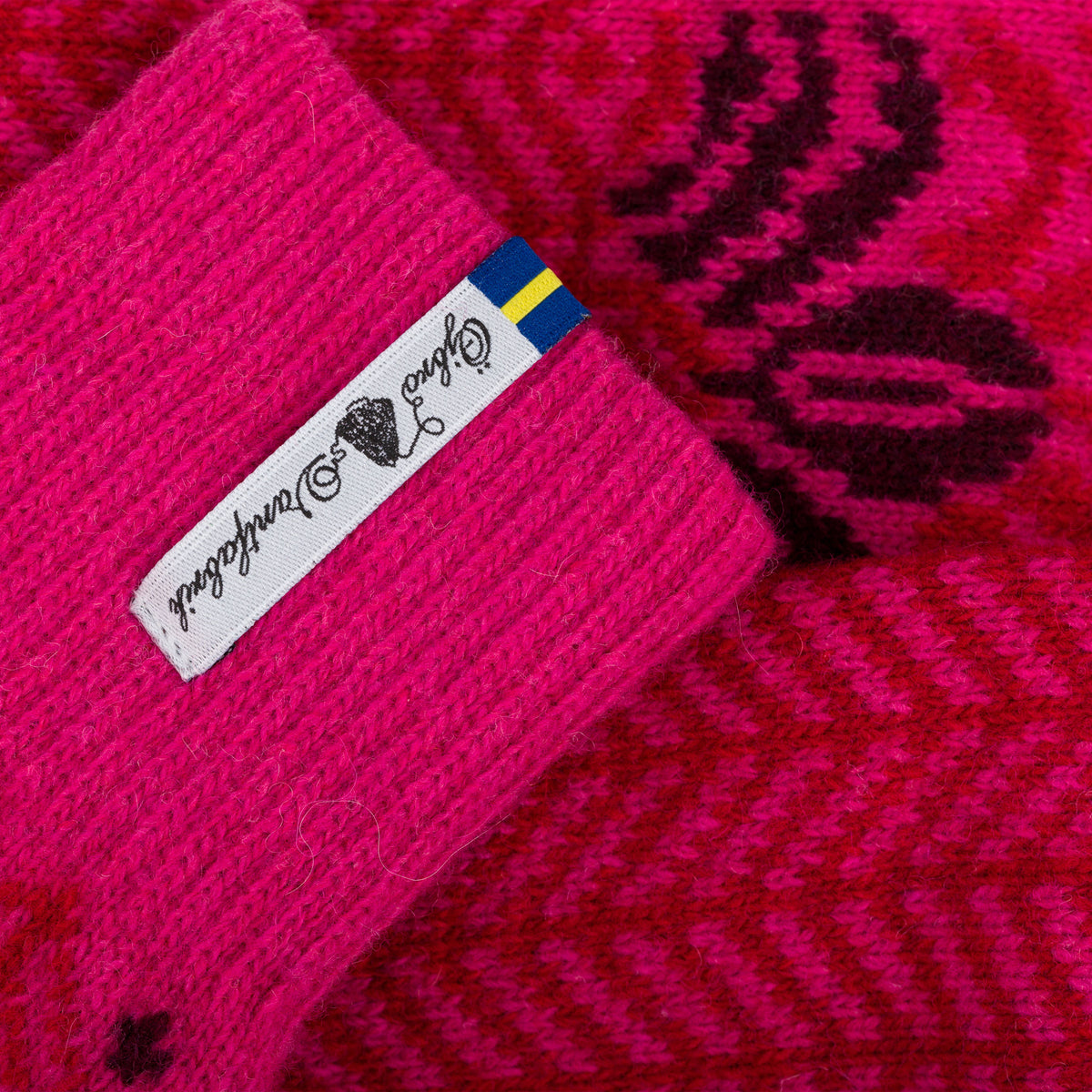 Close-up of a bright pink knit socks with a white fabric label and a small Swedish flag, showing the knit texture and patterned fabric.
