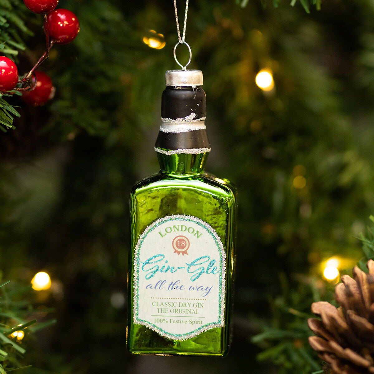 Green gin bottle ornament hanging on a Christmas tree with lights and pine cones.