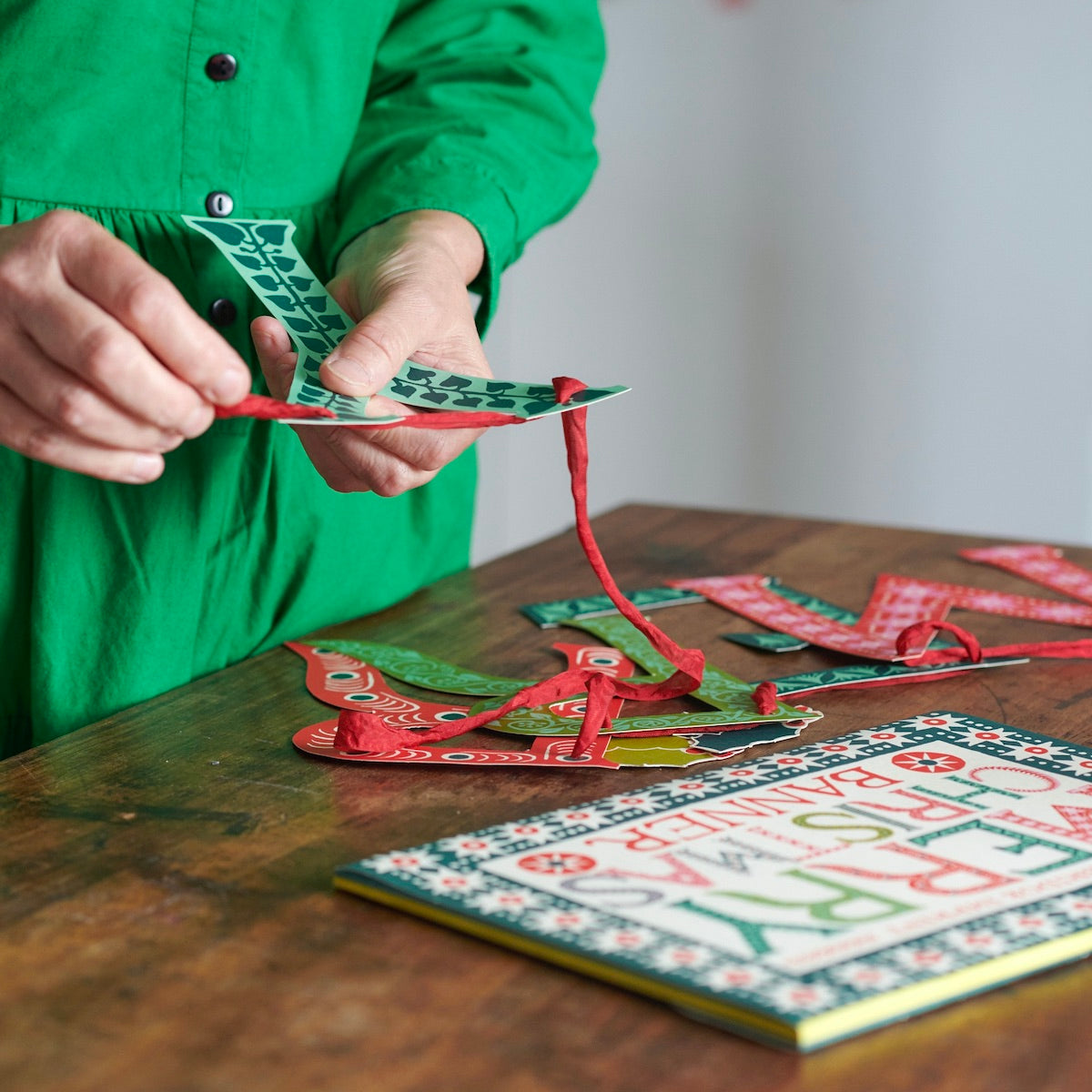 Person in a green shirt playing with colorful paper letters on a wooden table.