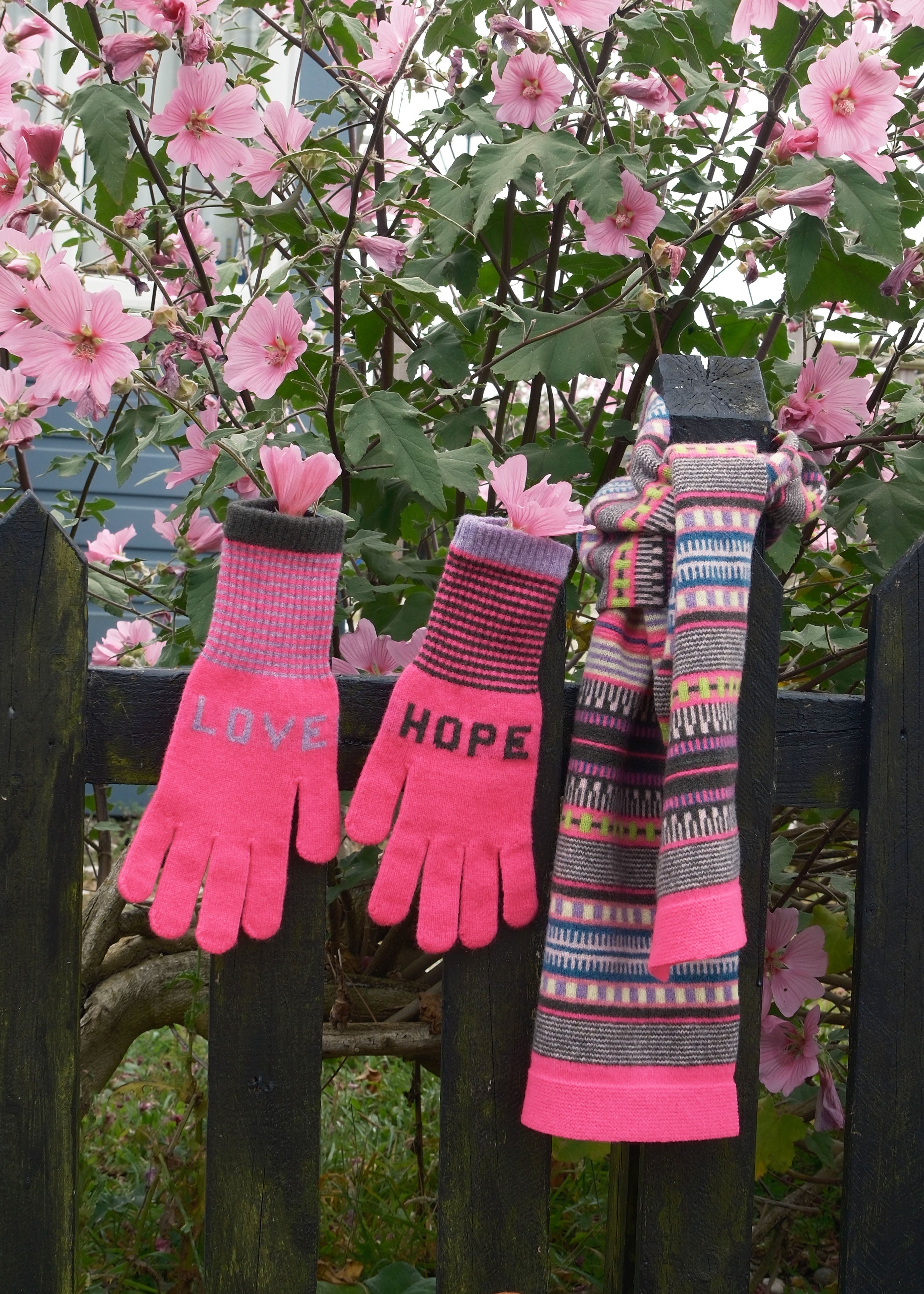 Pair of pink gloves with 'LOVE' and 'HOPE' text, and a patterned scarf against a floral background.