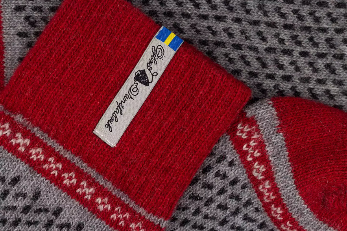 Close-up of a red knit sock with a white brand tag and a small Swedish flag, laid over a gray and black patterned knit textile.