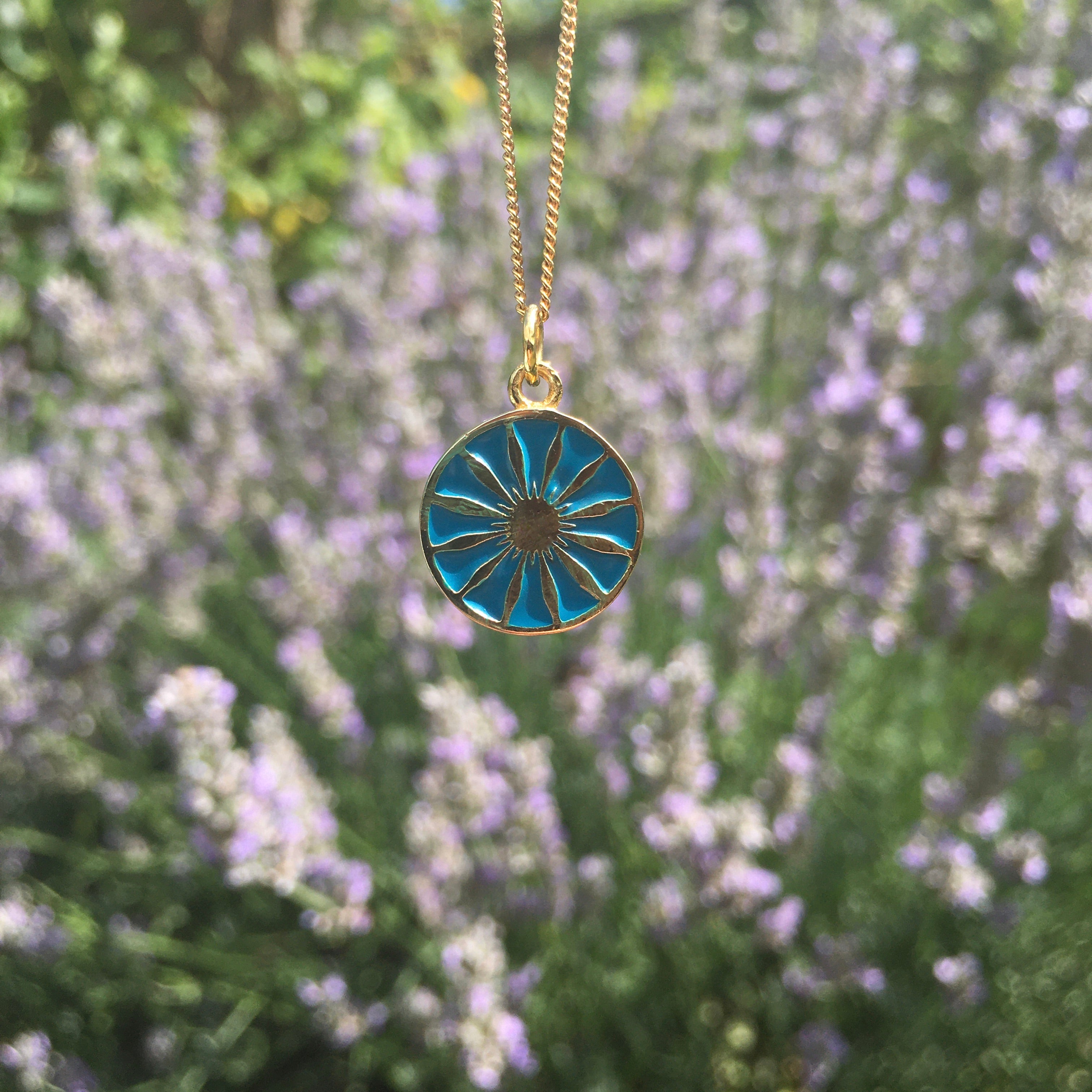 turquoise daisy medallion in gold vermeil in front of lavender
