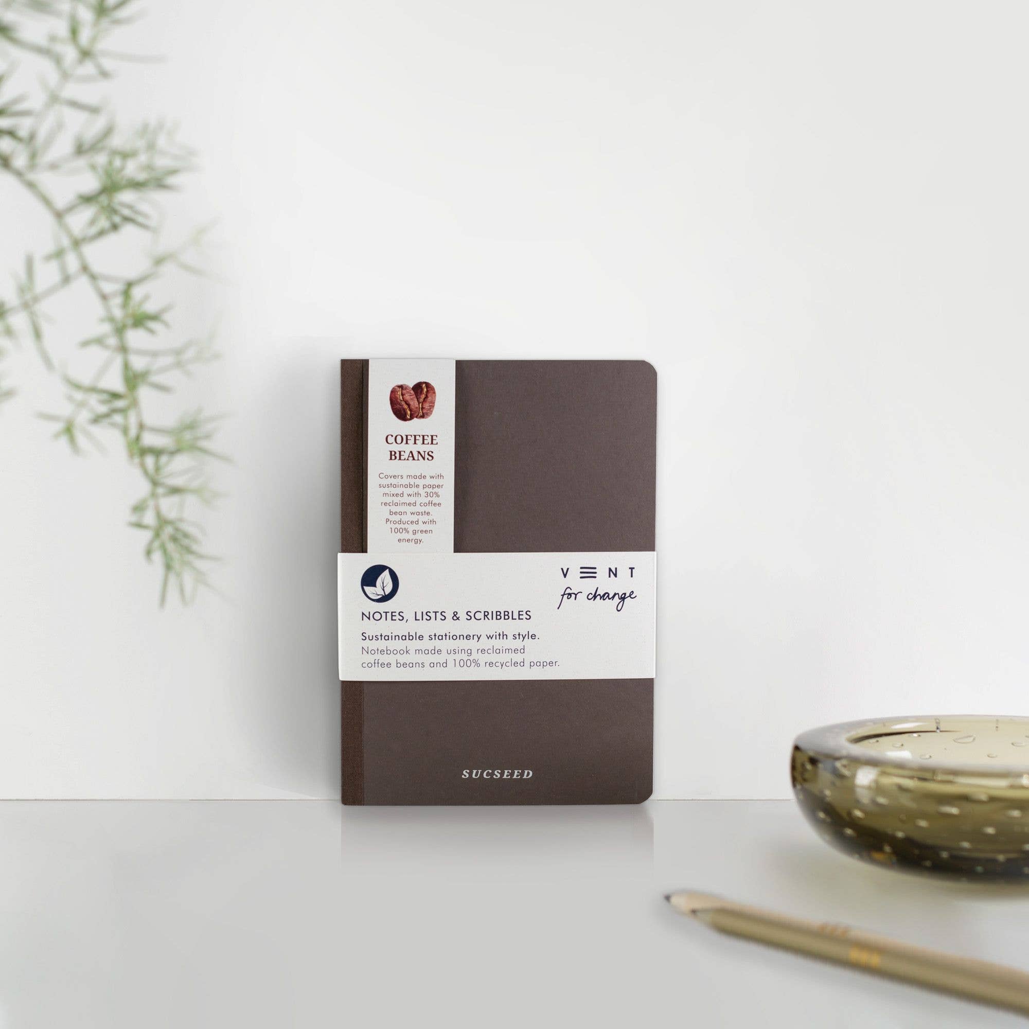 Brown notebook with white label on a light surface with a plant and candle in the background