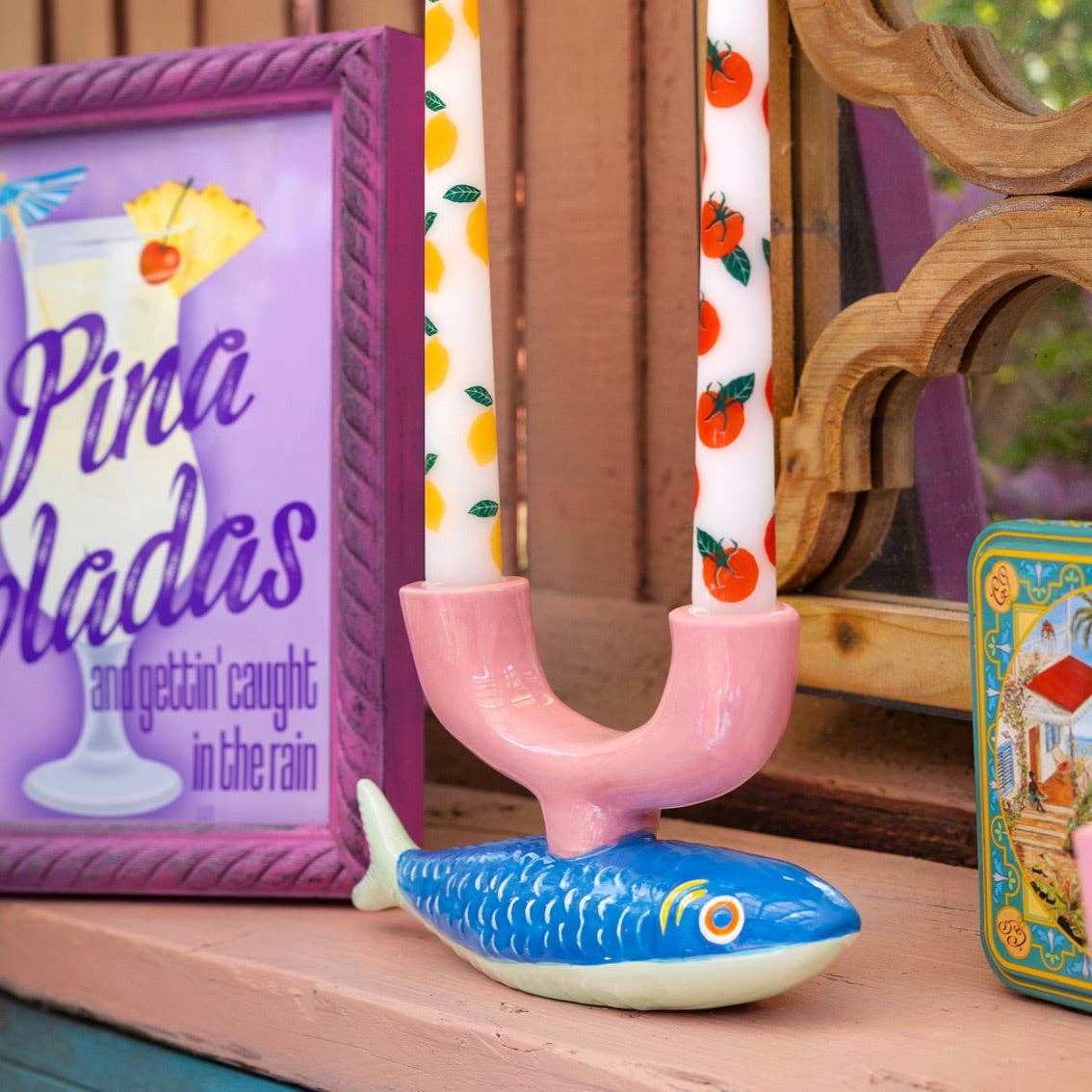 Pink toy fishbowl with a blue fish, candles, and a framed picture on a wooden surface.
