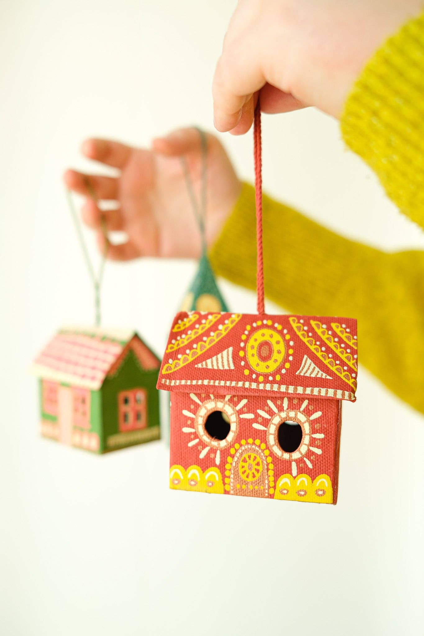 Hand holding a colorful birdhouse with another birdhouse in the background