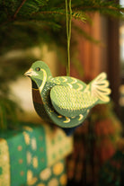 Decorative green dove ornament hanging on a tree with blurred gift box in the background