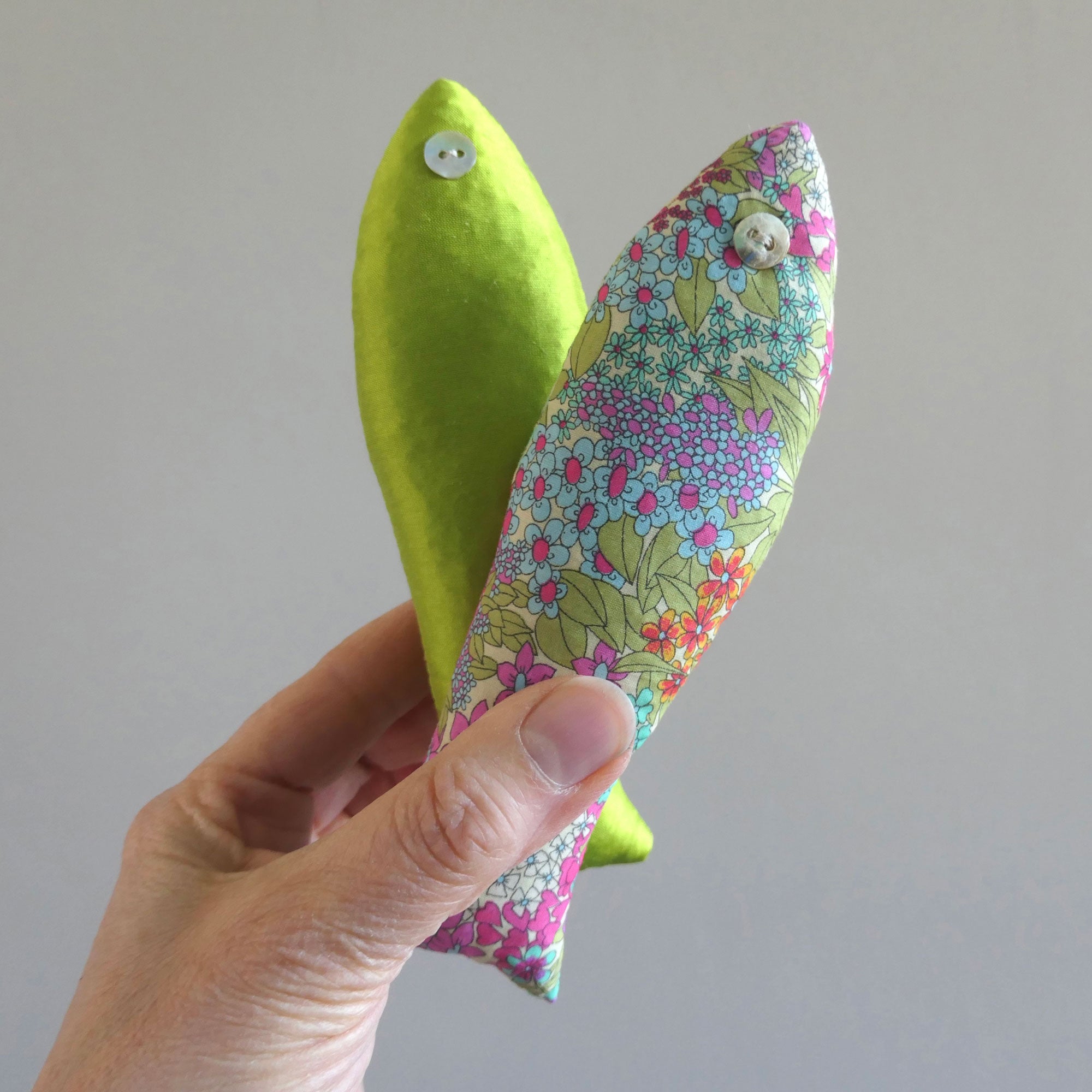 Hand holding a two cotton sachets in green and pink against a plain background