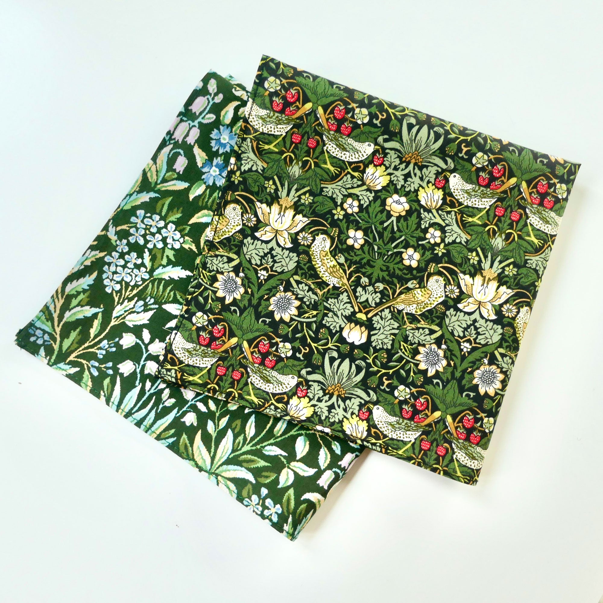 Two green fabric hankies with a floral and Strawberry Thief pattern on a white background