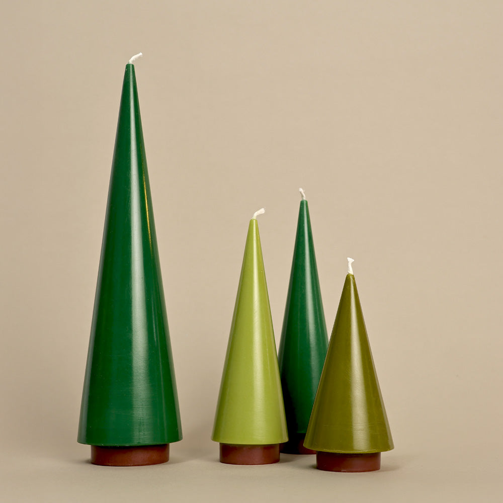 Four green tree-shaped candles with brown bases on a beige background