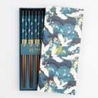 Showing the patterned box lid resting on top of the open chopsticks set featuring a crane print in teal