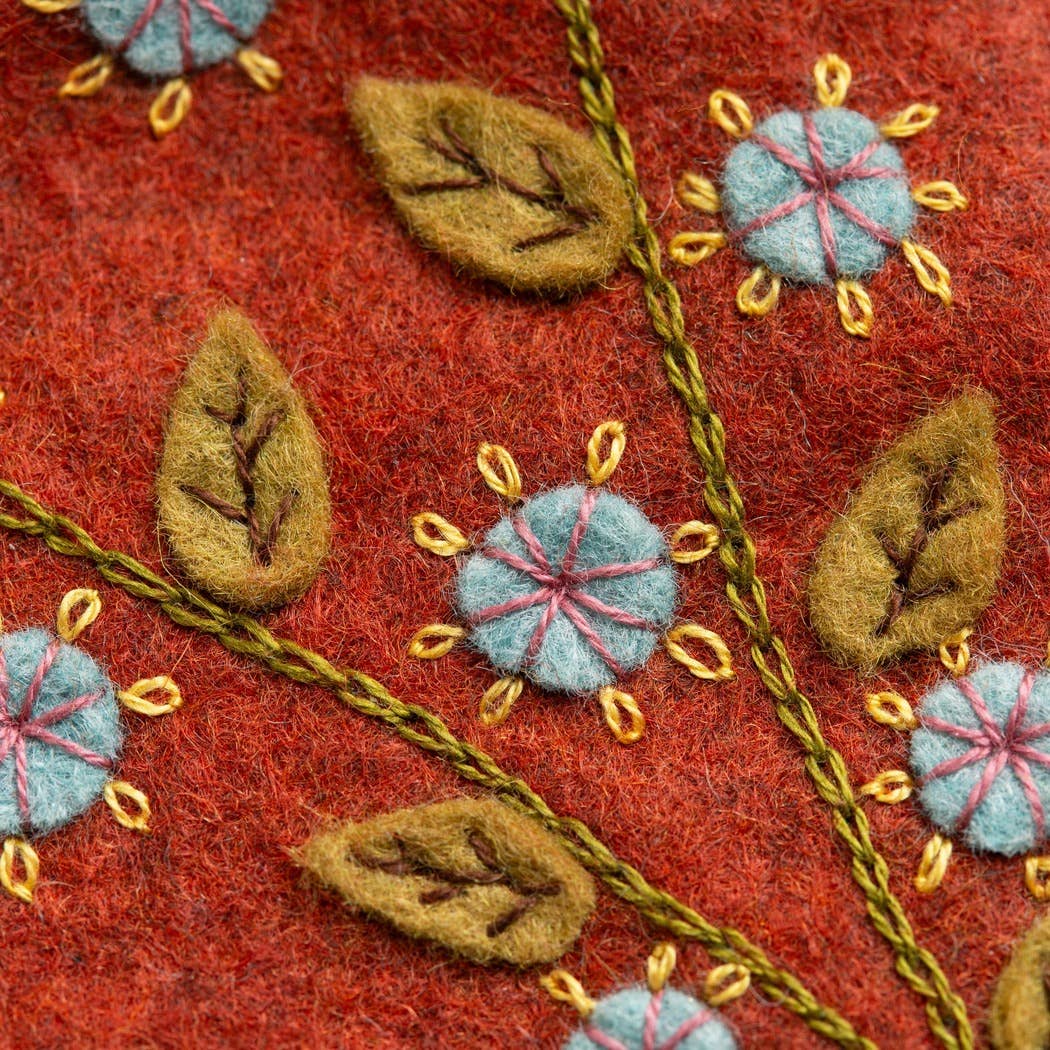 Detail of colourful red felt and botanical embroidery in blue, yellow, green and pink with olive green felt leaves and blue flower designs. 