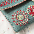 Close up of red, pink and yellow embroidery stitching on a light teal felt sewing pouch.