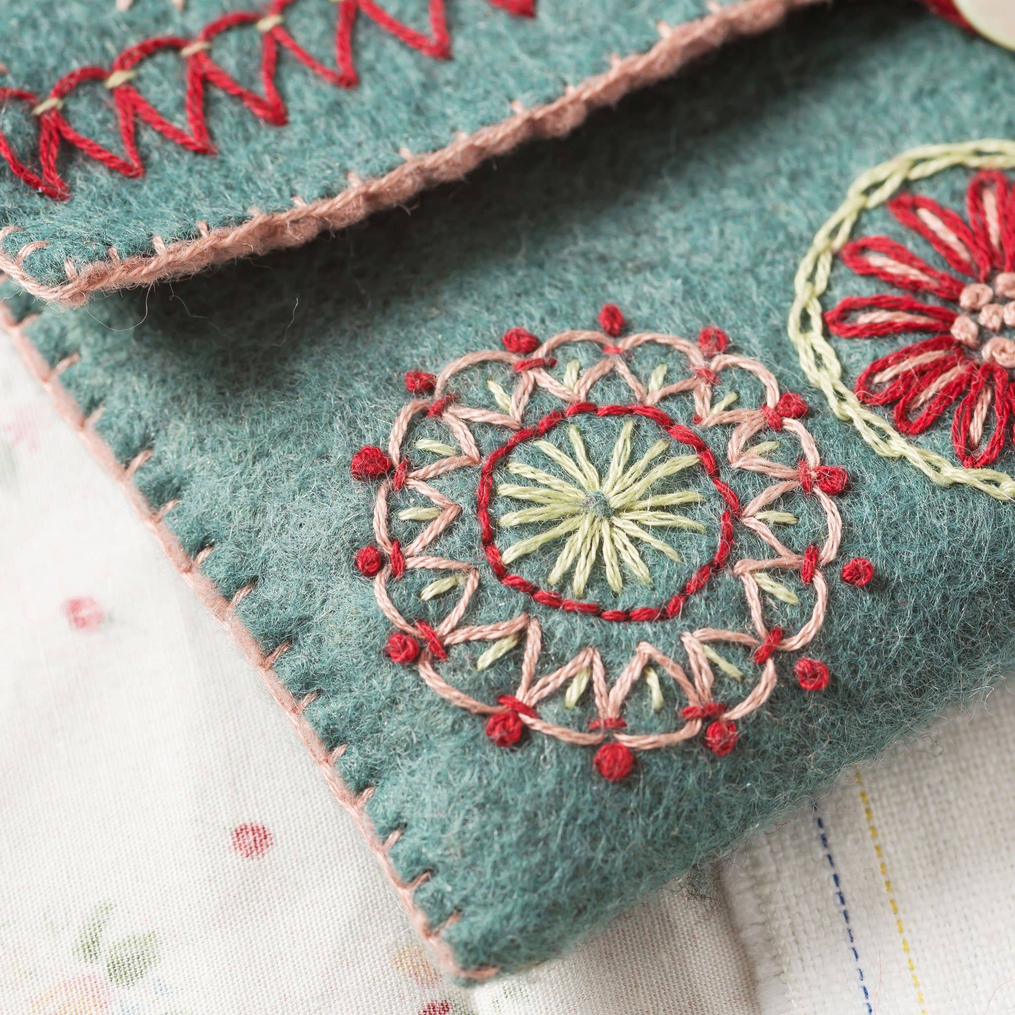 Close up of red, pink and yellow embroidery stitching on a light teal felt sewing pouch.