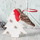 An embroidered red and brown felt robin with red ribbon loop displayed on a rustic scandi style wooden white tree.